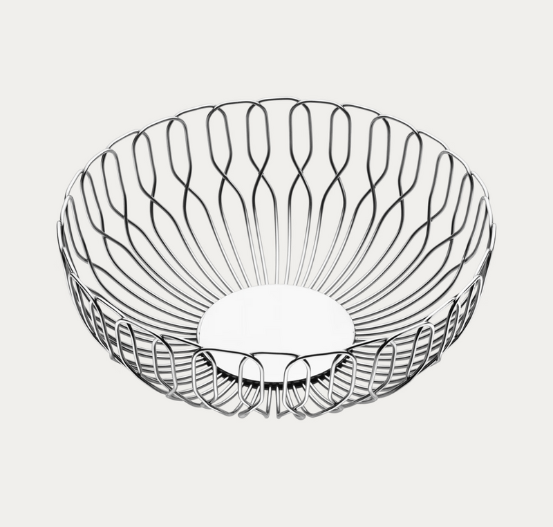 The Alfredo Bread Basket - Small by Georg Jensen is a round, open wire basket with a curved, sculptural design and a flat base, crafted from shiny stainless steel. Shown against a plain white background, this stylish piece is perfect for serving bread or fruit and adds a modern touch to any table setting.
