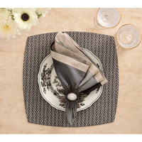 A square black-and-white Twill Placemat Set of 4 topped with a floral plate, a folded grey napkin, and a decorative starburst napkin ring.