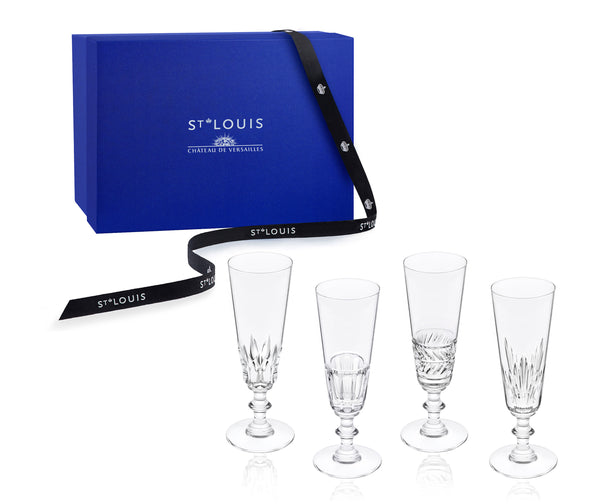 Four Saint Louis Queen’s Hall Champagne Flute- Set of 4 glasses with varied decorative patterns, displayed in front of a blue gift box wrapped with a branded ribbon.