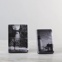 Two Simon Pearce Woodbury Photo Block Verticals sit on a marble surface. The left holds a black-and-white canal scene with a bridge, while the right displays a lighthouse and house, both in dramatic monochrome.