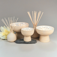 Blueme Balance Candles made from a soothing soy wax blend are arranged with reed diffusers on a gray surface, accented by a yellow flower and dark stone, set against a light gray background.