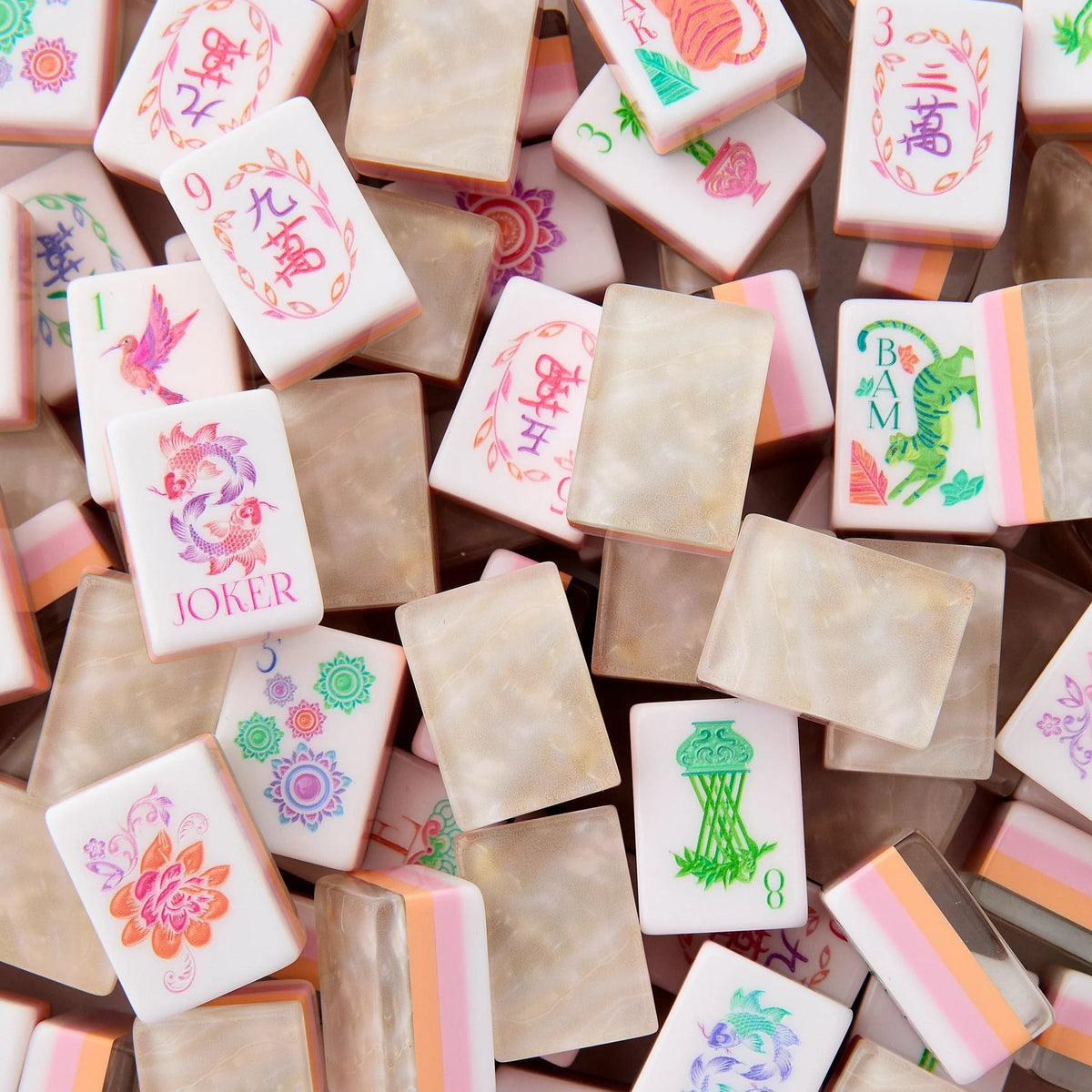 A vibrant pile of Oh My Mahjong’s Pearlescent Mahjong Tiles Set showcases colorful tiles with intricate designs, numbers, and symbols. Accented in pink, green, and orange hues, some tiles feature flowers, birds, or the word JOKER—evoking the lively charm of a floral mahjong set.
