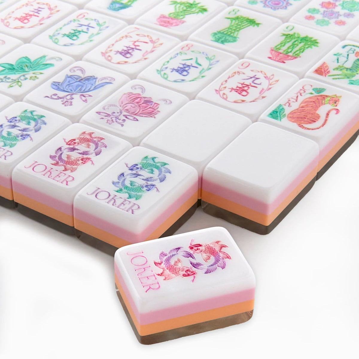 Oh My Mahjong’s Mahjong Tiles Set – Pearlescent features colorful floral tiles adorned with intricate animal motifs and JOKER tiles, echoing the elegance of a mother-of-pearl set. Layered pastel hues grace the sides of each pearlescent tile, arranged neatly on a white surface.