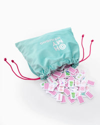 The Mahjong Debutante Travel Tile Set by Oh My Mahjong features a teal drawstring bag with pink cords, revealing colorful patterned tiles—perfect for introducing mahjong to kids anywhere.