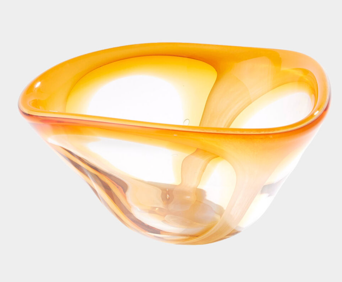 The Enigma Bowl - Amber by Global Views / Surya features a translucent, asymmetrical glass design with smooth curves and striking orange-yellow accents, shown against a plain white background.
