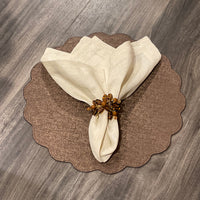 A cream-colored cloth napkin with a beaded ring rests on the Deborah Rhodes Victoria Round Scallop Placemat Set of 4, bringing elegance and easy care to your wooden table.