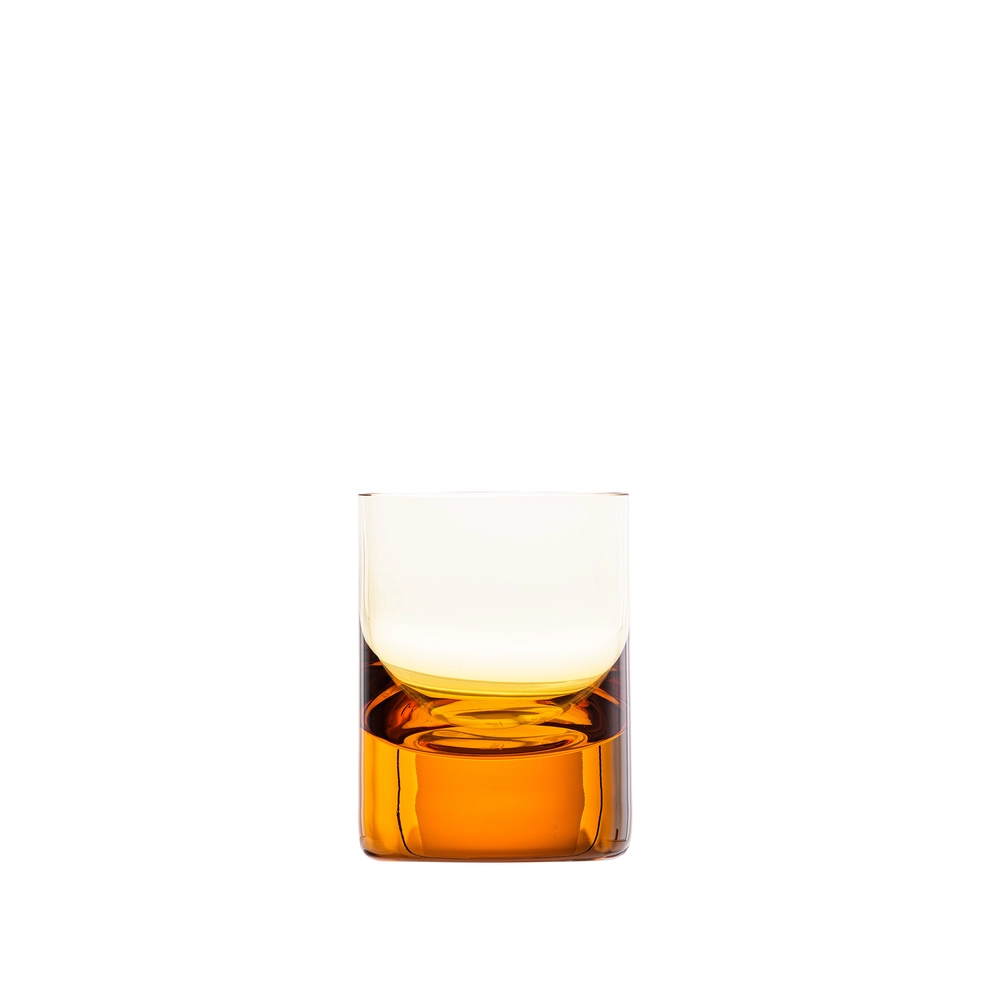 A clear, hand-blown Whiskey Set Shot Glass by Moser, filled with amber liquid—perhaps whiskey or another fine spirit—rests against a plain white background. The impeccable craftsmanship highlights the subtle artistry of custom engraving along its surface, lending a personal touch to this elegant glassware piece.