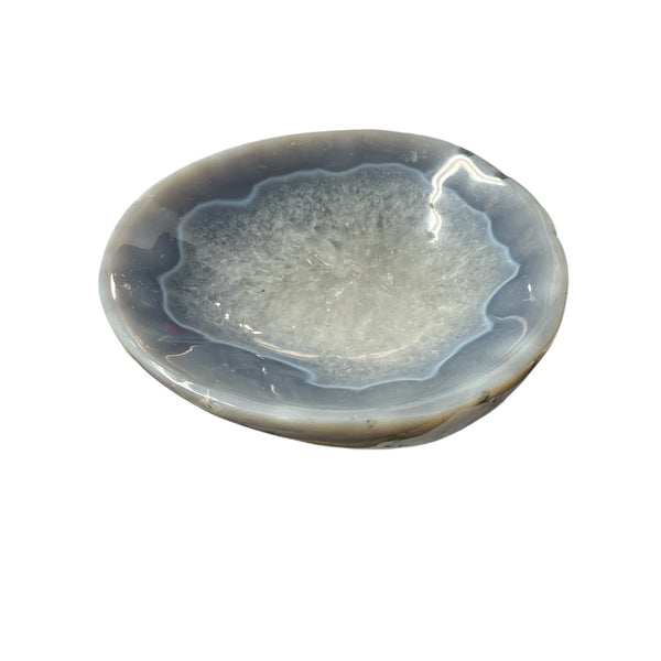 The Agate Bowl Brazil Blue by Verona Prive is a polished stone bowl with blue-gray banding and a crystalline center—a distinctive centerpiece on any white surface.