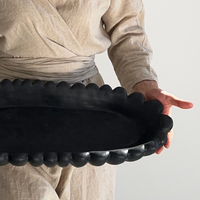 Person holding a black decorative tray with a textured rim against a plain background