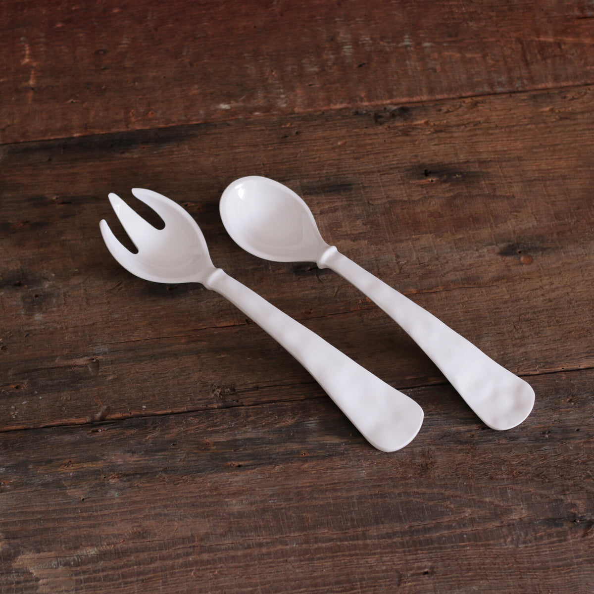 The Beatriz Ball Vida Havana Salad Servers - White, featuring one forked and one spoon-ended melamine server, are displayed side by side on a rustic wooden surface. These servers are decorative, practical, and dishwasher safe.