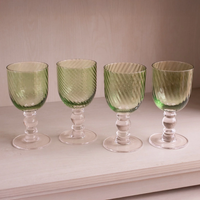 A set of four Beatriz Ball GLASS French Swirl Wine Set of 4 - Green glasses, each featuring a green swirl pattern and clear, multi-tiered stems, standing in a row.