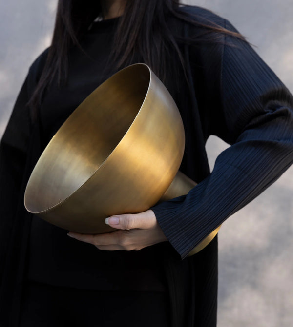 A person in dark clothing holds the Dumae Kara Brass Footed Bowl with both hands against a neutral, blurred background, showcasing the handcrafted artistry and elevated design of this artisan home decor piece.