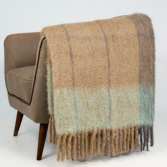 The Mantas Ezcaray Twist Frame Throw, in beige and light blue mohair, is draped over a light brown upholstered chair with wooden legs, set against a plain white background.