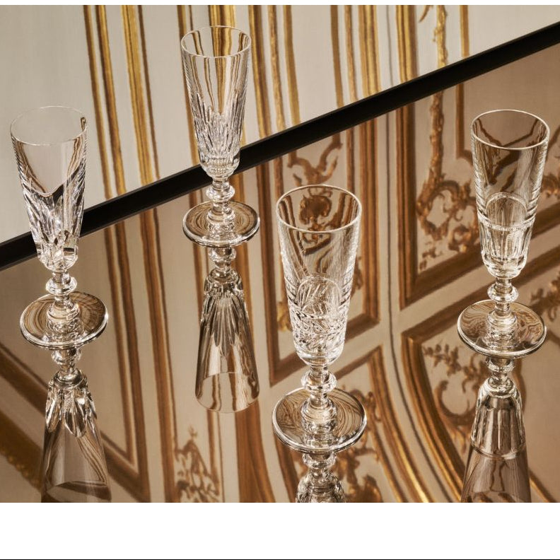 Four Saint Louis Queen’s Hall Champagne Flute- Set of 4 glasses with intricate cut glass patterns standing on a mirrored surface.