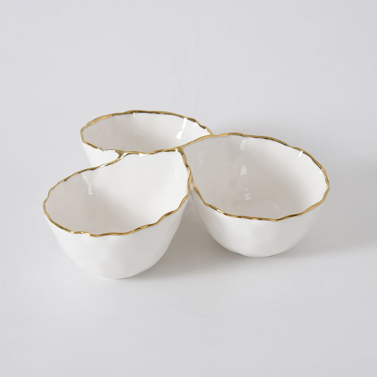 Three connected white porcelain bowls from PAMPA BAY’s Portofino Gold 3 Section Server, each adorned with uneven gold trim, are arranged in a cluster on a plain white background. This elegant server is perfect for stylish entertaining.