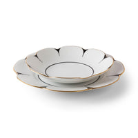 Two white Drops Dinnerware plates by Molecot, crafted from porcelain with scalloped flower-shaped edges, are stacked together. Each plate is adorned with a fine gold-finished rim and a delicate black accent outlining the edges. The background is pure white.