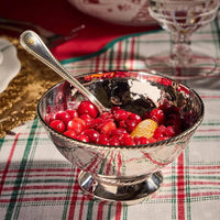The Juliska Graham Cocktail Bowl, crafted from hammered stainless steel, is filled with cranberry sauce and orange slices on a plaid tablecloth, with a silver spoon resting inside.