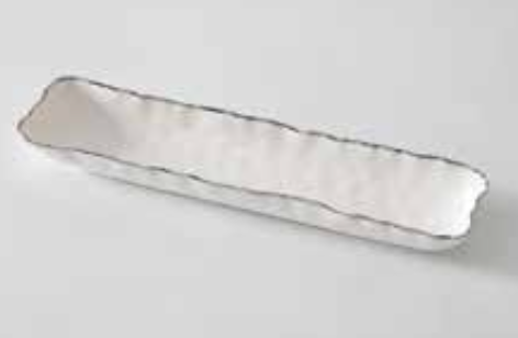 The Portofino Plata Cracker Tray by PAMPA BAY is a long, narrow white ceramic dish with wavy edges and a silver trim, displayed on a light gray surface.