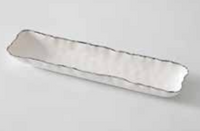 The Portofino Plata Cracker Tray by PAMPA BAY is a long, narrow white ceramic dish with wavy edges and a silver trim, displayed on a light gray surface.
