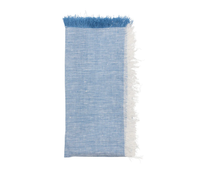 A folded natural chambray napkin from the Kim Seybert Chambray Fringe Napkin Set of 4, featuring a frayed edge and a strip of white fringe along one side, placed against a white background.