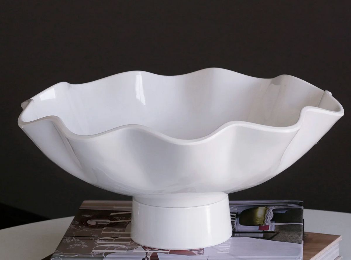 The Beatriz Ball Vida Havana Carola Pedestal Bowl White - Large, featuring wavy edges in luxury melamine, rests atop two stacked books against a dark background, creating an elegant centerpiece.