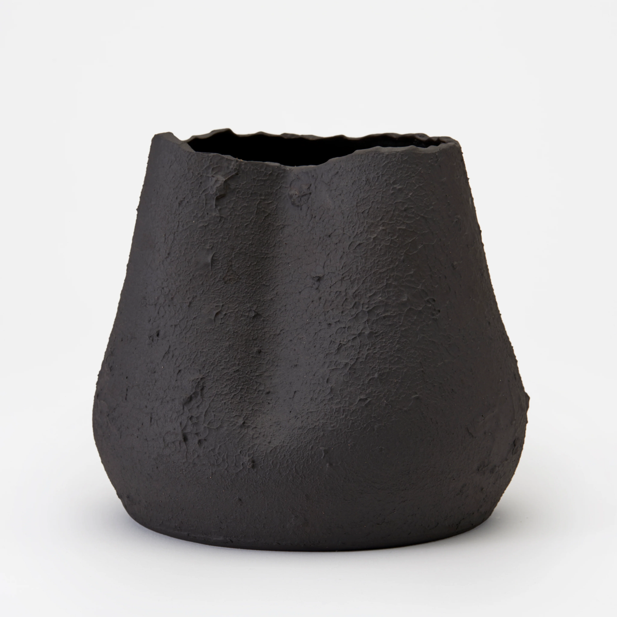 The Phoebe Vase by Dumae features a black matte finish, uneven textured surface, and an irregular wavy rim, highlighting its sculptural design against a plain white background.