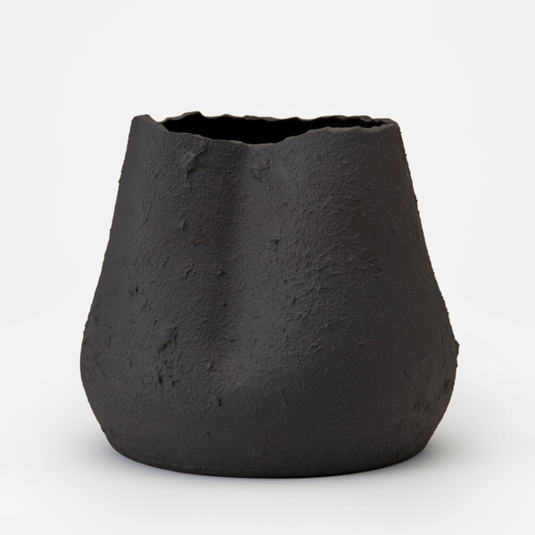 The Phoebe Vase by Dumae features a black matte finish, uneven textured surface, and an irregular wavy rim, highlighting its sculptural design against a plain white background.