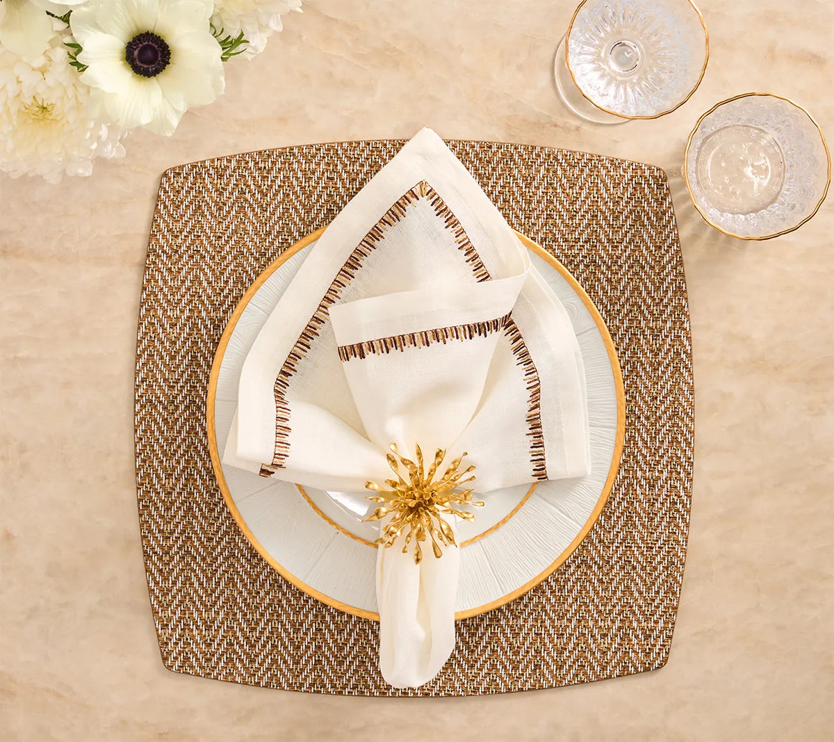 A Twill Placemat Set of 4 - Brown & White topped with a white plate, a folded napkin secured by a gold starburst napkin ring, and two glasses.