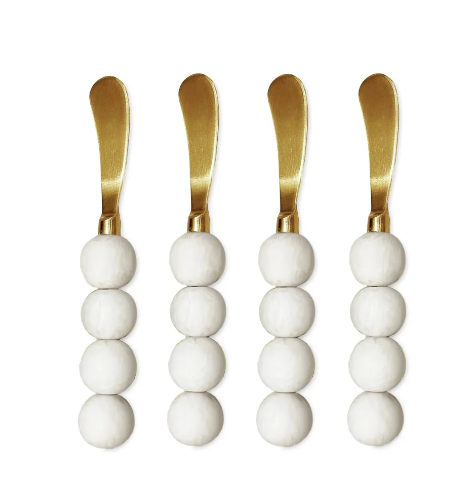 Four coconut-colored Resin Sorbet Spreaders by Beatriz Ball, each featuring a handle made of three stacked white spheres reminiscent of ceramic or marble, are arranged in a row on a white background. This set of four is perfect for dessert service.