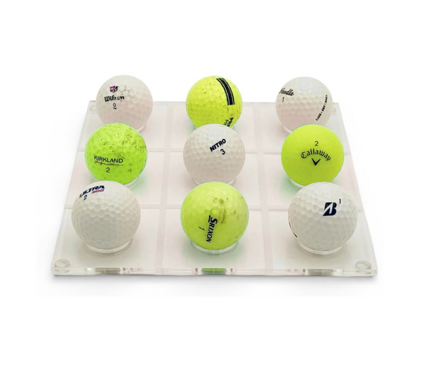 The Luxe Dominoes Golf Ball Tic Tac Toe set features nine white and yellow golf balls from different brands, arranged in a 3x3 lucite grid—each with visible logos and numbers, making it a perfect gift for golf lovers.