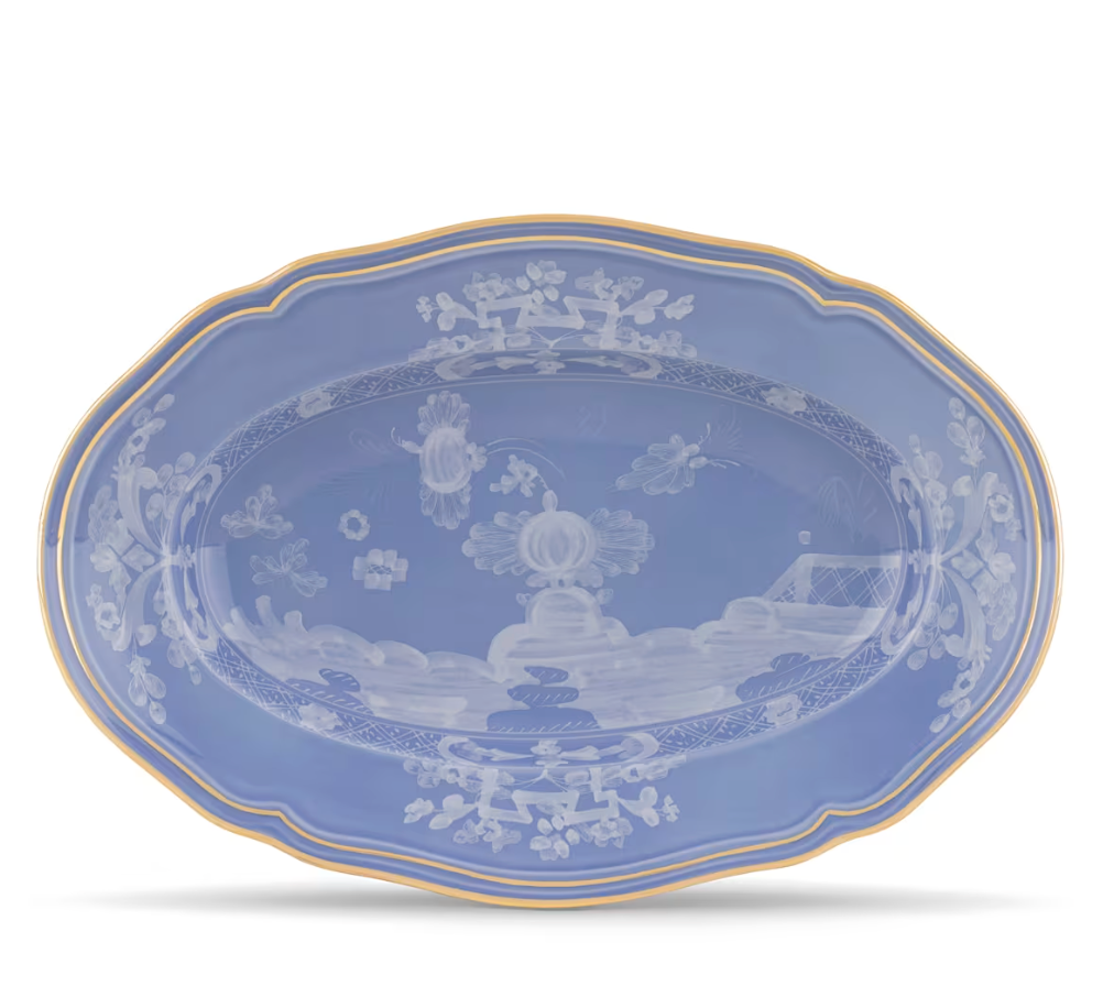 The Oriente Italiano Pervinca by Ginori 1735 is a blue oval ceramic platter with scalloped edges, a white floral and landscape pattern, and a 24-karat gold rim, evoking classic elegance.