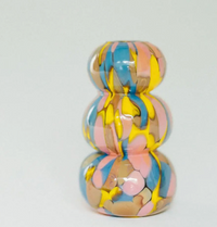 Introducing the Jelly Baby Mini Vase Collection by Maria Ida Designs—a handmade art glass vase featuring a glossy, three-tiered abstract form with swirled patterns of yellow, blue, pink, and beige. Set against a plain light gray background, this unique piece makes for truly distinctive home decor.