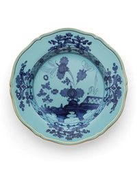 Light blue Ginori 1735 Oriente Italiano Dinnerware Iris porcelain plate with a scalloped edge, gold trim, and dark blue chinoiserie floral and landscape patterns.