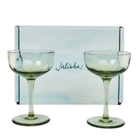 Two light green Juliska Puro Cocktail Coupes (set of 2) are displayed in front of a light blue, gift-boxed set featuring the brand’s elegant cursive logo—perfect for serving stylish cocktails.