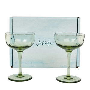 Two light green Juliska Puro Cocktail Coupes (set of 2) are displayed in front of a light blue, gift-boxed set featuring the brand’s elegant cursive logo—perfect for serving stylish cocktails.
