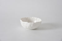 The PAMPA BAY Willow White Bowl, featuring a wavy rim and white ceramic finish, sits on a smooth light gray surface with a plain light gray background.