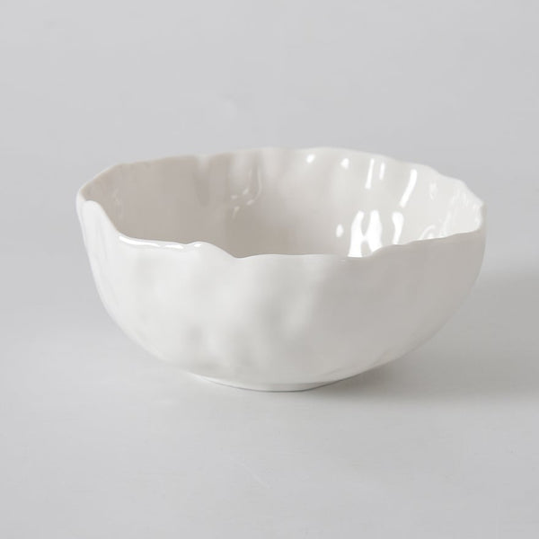 The PAMPA BAY Willow White Bowl, featuring a wavy rim and white ceramic finish, sits on a smooth light gray surface with a plain light gray background.