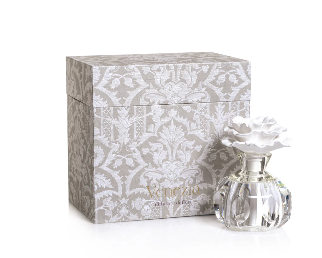 Alessandra Diffuser with a white ceramic flower top on a glass base, sitting in front of a patterned gray gift box labeled Venezia, diffusore di fiori.