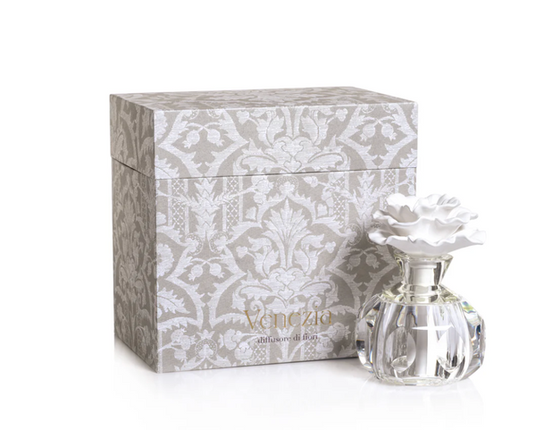 Alessandra Diffuser with a white ceramic flower top on a glass base, sitting in front of a patterned gray gift box labeled Venezia, diffusore di fiori.