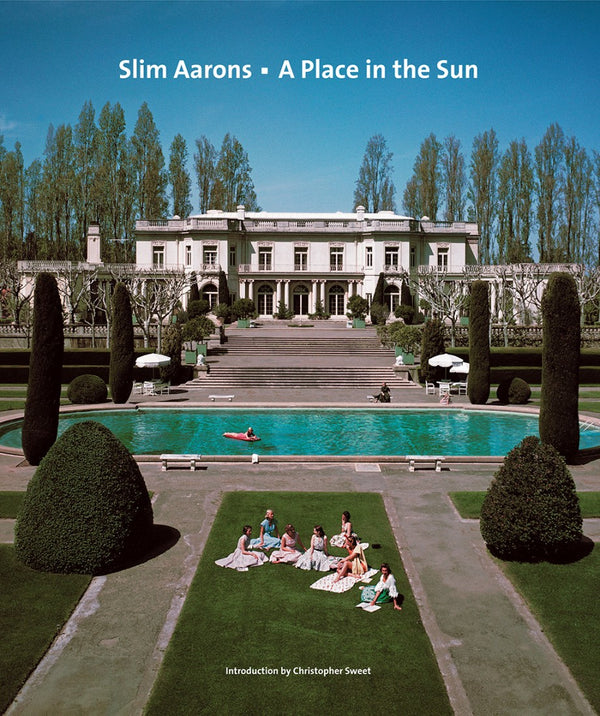Captured by Slim Aarons, “A Place In The Sun” features a grand mansion, gardens, and pool with people relaxing under a clear sky. Available from Abrams/Hachette Books.