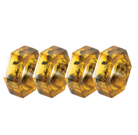 The Piper Napkin Rings, Tortoise Set of 4 by Bodrum are arranged in a row on a white background, highlighting the contemporary appeal of these modern napkin rings with their hexagonal shape and dark tortoise-patterned inclusions.
