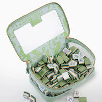 An elegant set, the Oh My Mahjong “Mahjong Tiles Set - Willow” features stacked green and cream tiles, some artfully scattered outside its green and clear zippered case adorned with a peacock design.