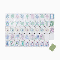 Mahjong tiles from the Oh My Mahjong Mahjong Tiles Set - Willow are arranged in rows, displaying circles, bamboo, characters, dragons, winds, flowers, and joker tiles. Among the floral tiles of this elegant set, a single green blank tile appears at the bottom right.