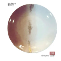 A round porcelain plate by Marie Daâge with a gold, brown, and white gradient design and a central gold stripe. Hand-painted in France. Current Home logo at top left; "48 Horizon Gold" at bottom right. Product: Marie Daâge Horizon Gold Dinnerware.