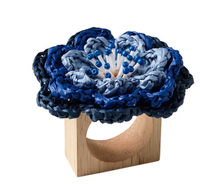 The Kim Seybert Pareo Napkin Ring Set of 4 in Periwinkle & Blue features square wooden rings adorned with large, braided blue and navy flowers, accented by blue beads at the center.