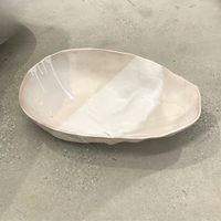 The Ripple Oval Large Bowl by Alex Marshall Studios is a handmade ceramic piece with an irregular shape and glossy off-white finish, ideal as an oversized serving bowl for salads.