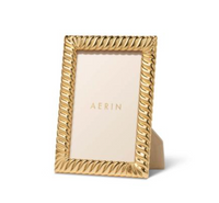 The Aerin Loretta Frame Gold features a textured, twist design and stands upright on a white surface. It holds a placeholder card with "AERIN" in gold letters and fits a 4x6 photo.