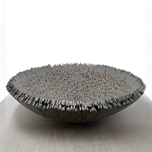 The Boracay Centerpiece Bowl by Quilted Koala, a large handcrafted decorative piece featuring numerous vertical metal rods of varying heights that form a spiky, textured rim, sits on a light-colored wooden surface against a plain white background.