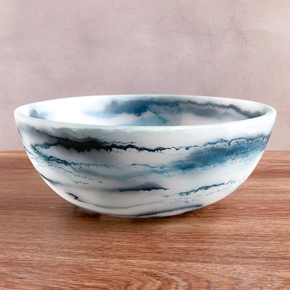 The Redondo Bowl - Blue Swirl by CDMX / PAOLA VALLE features swirling blue marbled patterns, bringing Italian-inspired charm to a wooden surface against a light beige background.