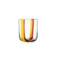 A Gesti Tumbler by Ichendorf Milano, featuring clear glass with yellow and red curved stripes running vertically from the rim to the base, set against a white background.